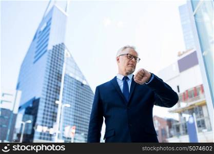 business, punctuality and people concept - senior businessman checking time on wristwatch or smart watch on his hand in city. senior businessman checking time on his wristwatch