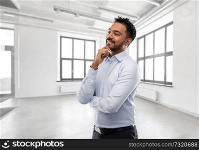 business, realty and people concept - smiling indian businessman or realtor over empty office room background. indian businessman or realtor in empty office room