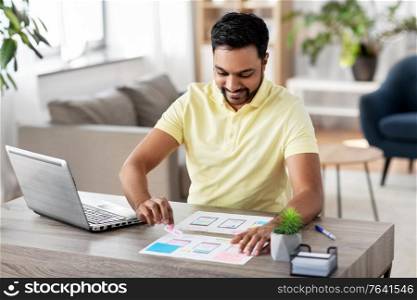 business, remote job and technology concept - happy smiling male ui designer with laptop computer working on user interface design at home office. ui designer working on user interface at home