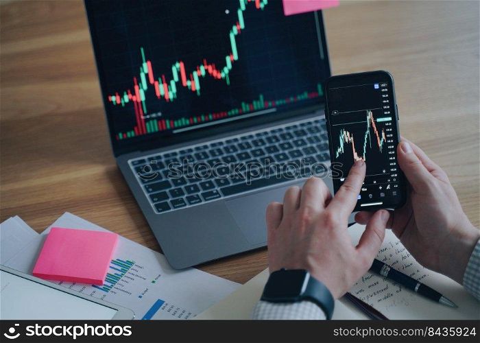 Business report. Financial diagram is on laptop and smartphone screens. Man is working on the deal in office. Mobility and Online trading. Display of PC and phone on the desk. Startup development.. Business report. Financial diagram is on screens. Man is working on the deal. Startup development.