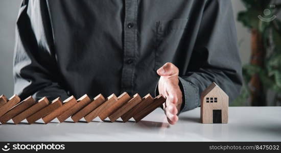 Business risk plan real estate protection. Man hand blocks wood block from many row falling wooden block like domino to house model, Insurance ideas to prevent loss concept