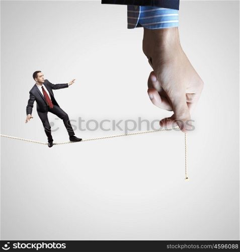 Business risks. Young businessman balancing on rope controlled by male hand