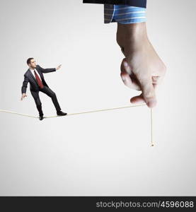 Business risks. Young businessman balancing on rope controlled by male hand