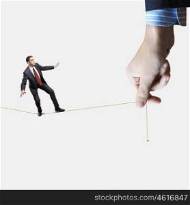 Business risks. Young businessman balancing on rope controlled by male hand