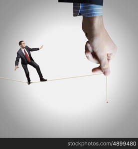 Business risks. Young businessman balancing on rope controlled by male hand