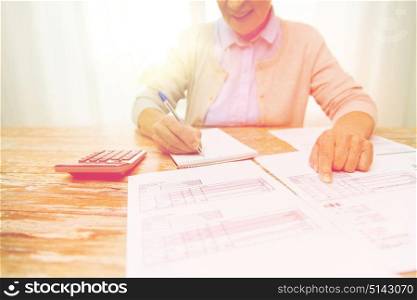 business, savings, annuity insurance, age and people concept - close up of senior woman with papers or bills and calculator writing at home. senior woman with papers and calculator at home