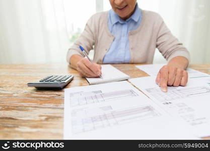 business, savings, annuity insurance, age and people concept - close up of senior woman with papers or bills and calculator writing at home