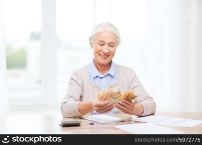 business, savings, annuity insurance, age and people concept - happy senior woman with calculator and bills counting euro money at home