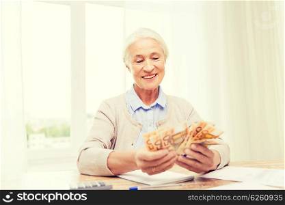 business, savings, annuity insurance, age and people concept - happy senior woman with calculator and bills counting euro money at home