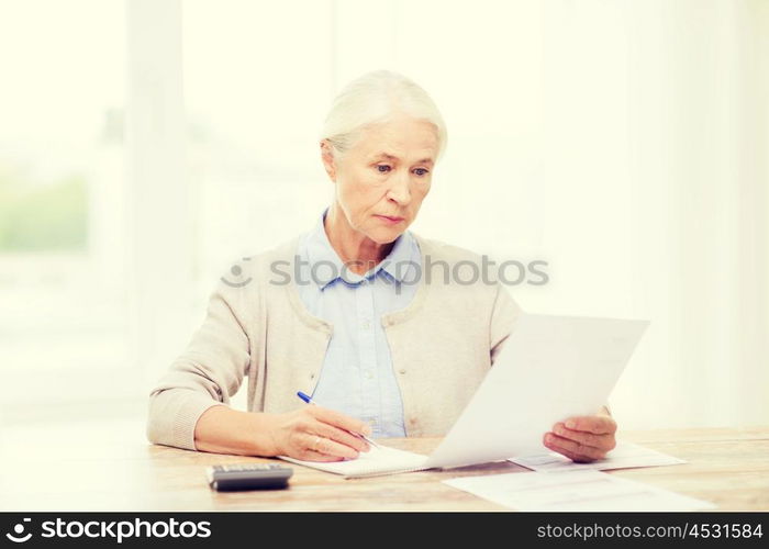 business, savings, annuity insurance, age and people concept - senior woman with papers or bills and calculator writing at home