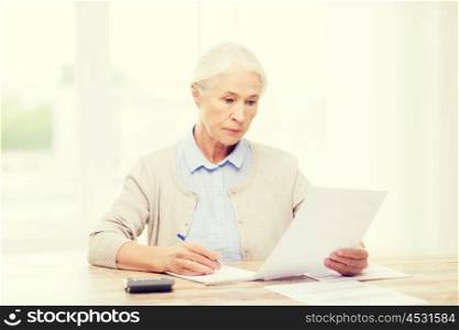 business, savings, annuity insurance, age and people concept - senior woman with papers or bills and calculator writing at home