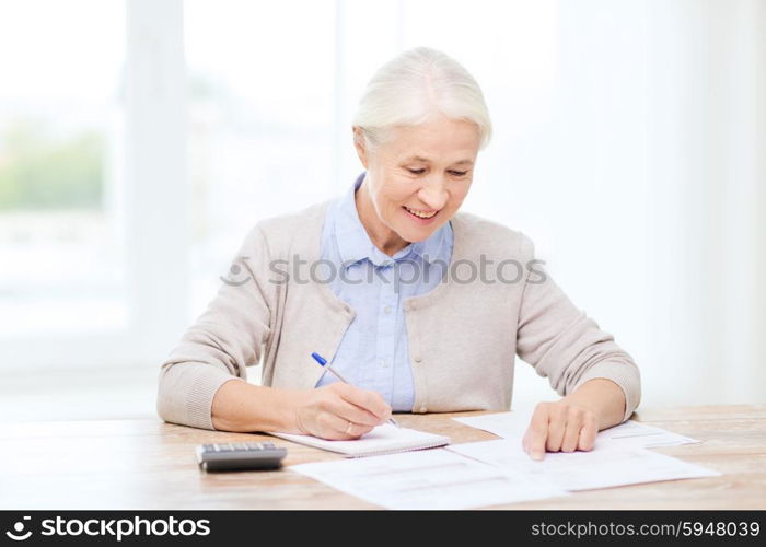 business, savings, annuity insurance, age and people concept - senior woman with papers or bills and calculator writing at home