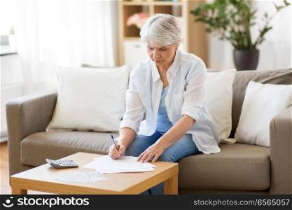 business, savings, annuity insurance, age and people concept - senior woman with papers or bills and calculator writing at home. senior woman with papers and calculator at home