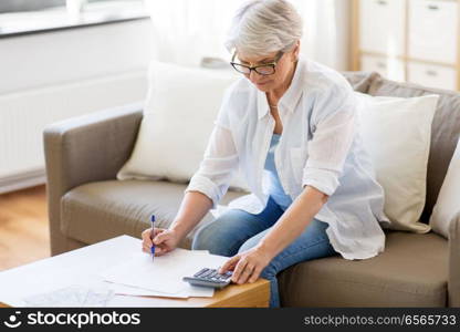 business, savings, annuity insurance, age and people concept - senior woman with papers or bills and calculator writing at home. senior woman with papers and calculator at home