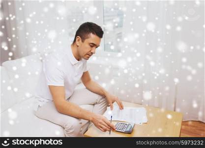 business, savings, finances and people concept - man with papers and calculator at home counting and filling tax form over snow effect