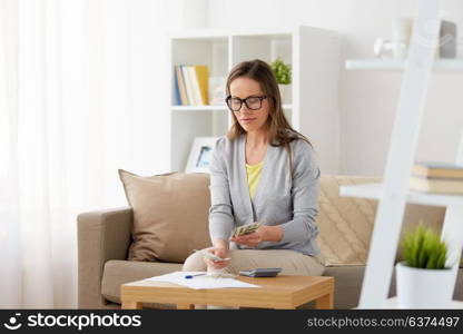 business, savings, finances and people concept - middle-aged woman with papers and calculator counting money at home. woman with calculator counting money at home