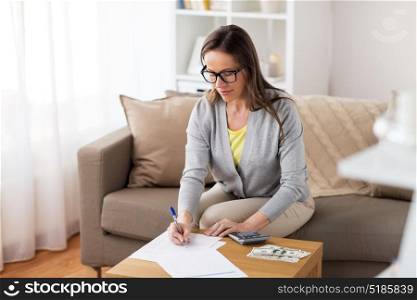 business, savings, finances and people concept - woman with money, papers and calculator at home. woman with money, papers and calculator at home