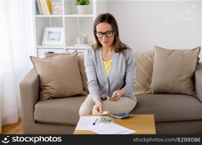 business, savings, finances and people concept - woman with papers and calculator counting money at home. woman with papers counting money at home