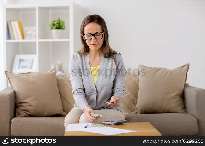 business, savings, finances and people concept - woman with papers and calculator counting money at home. woman with papers counting money at home