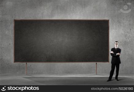 Business seminar. Young businessman in glasses and blank blackboard