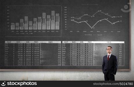 Business seminar. Young confident man wearing glasses standing near blackboard