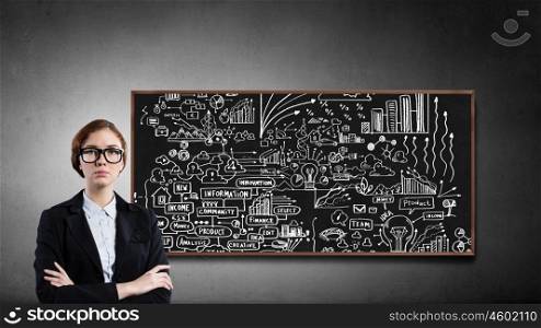 Business seminar. Young confident woman wearing glasses standing near blackboard
