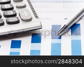Business silver pen and calculator over office charts close-up
