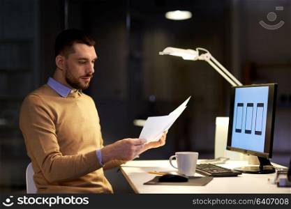business, software development, deadline and technology concept - man with papers and user interface mockup on computer screen working at night office. man with papers and computer works at night office