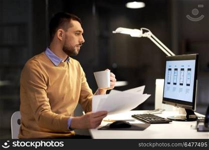 business, software development, deadline and technology concept - man with papers, coffee and user interface mockup on computer screen working at night office. man with papers and computer works at night office. man with papers and computer works at night office