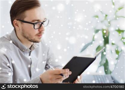 business, startup and people concept - businessman or creative male office worker with book or diary and pen at home office over snow