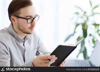 business, startup and people concept - businessman or creative male office worker with book or diary and pen at home office