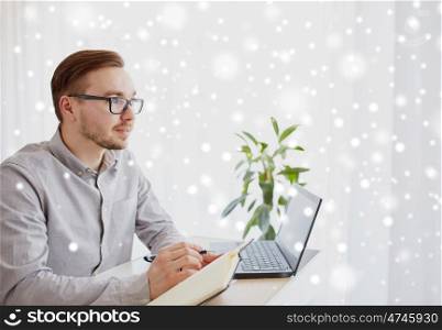 business, startup and people concept - businessman or creative male worker writing to notebook or diary with pen at home office over snow