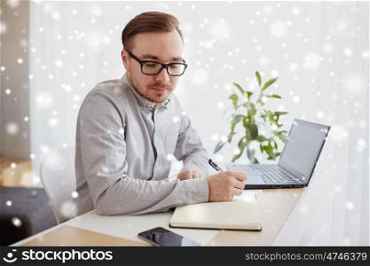 business, startup and people concept - businessman or creative male worker writing to notebook or diary and looking at smartphone at home office over snow