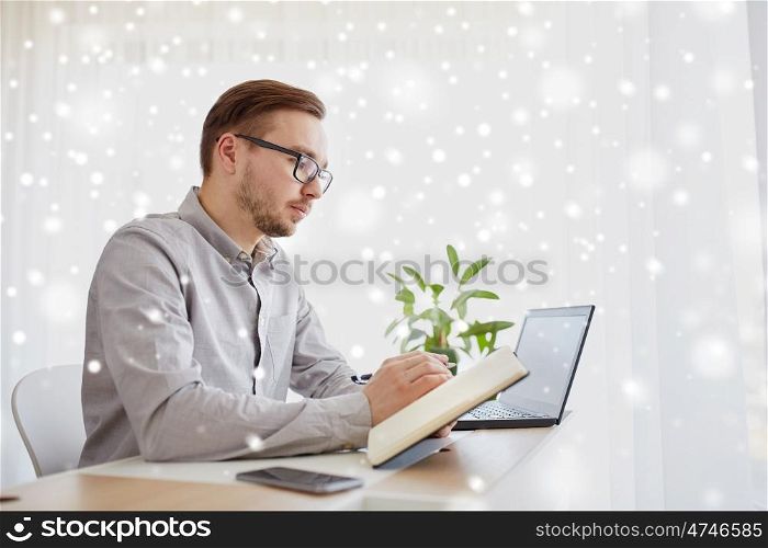business, startup and people concept - businessman or creative male worker writing to notebook or diary with pen at home office over snow
