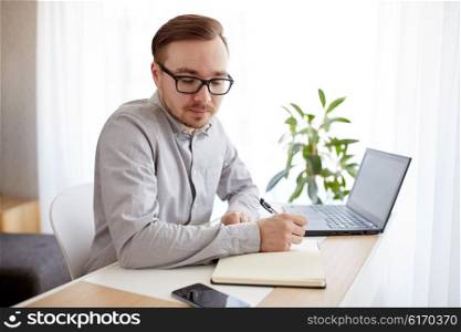 business, startup and people concept - businessman or creative male worker writing to notebook or diary and looking at smartphone at home office
