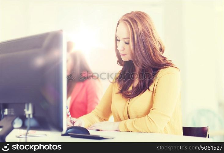 business, startup and people concept - businesswoman or creative female office worker with computer writing to notebook. creative female office worker writing to notebook