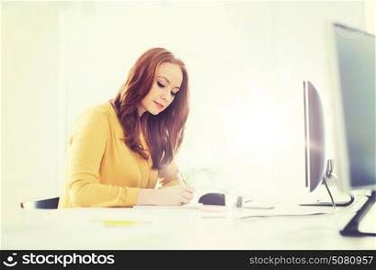 business, startup and people concept - businesswoman or creative female office worker with computer writing to notebook. creative female office worker writing to notebook