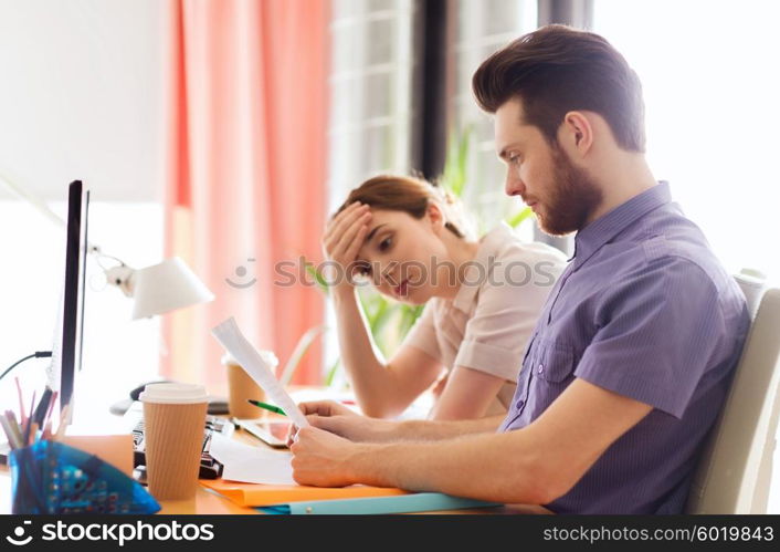 business, startup and people concept - creative team of man and woman with computer and files solving problem in office