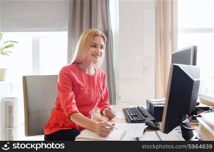 business, startup and people concept - happy businesswoman or creative female office worker with computers writing to notebook