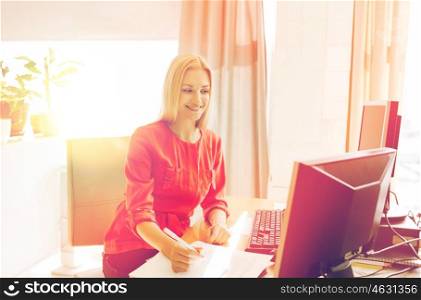 business, startup and people concept - happy businesswoman or creative woman with computers writing to notebook at office