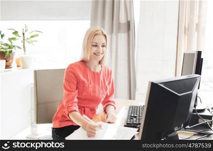 business, startup and people concept - happy businesswoman or creative woman with computers writing to notebook at office