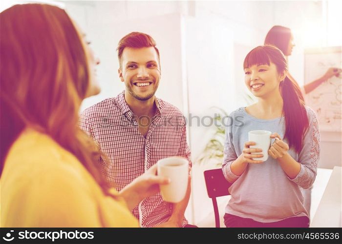 business, startup and people concept - happy creative team or students drinking coffee and talking at office