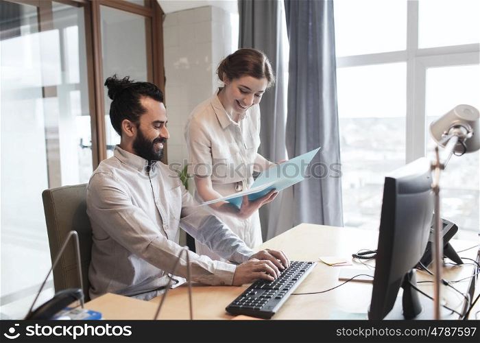 business, startup and people concept - happy creative team with computer and folder in office