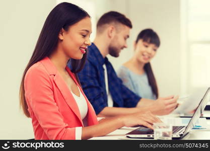 business, startup, education and people concept - happy young african woman typing on laptop computer over creative team or students working at office. happy african woman over creative team at office