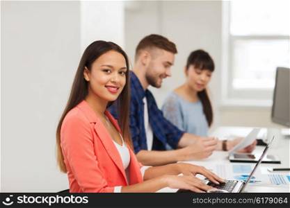 business, startup, education and people concept - happy young african woman typing on laptop computer over creative team or students working at office