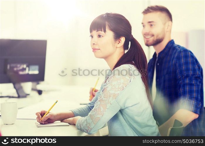 business, startup, education and people concept - happy young asian woman with notebook and pencil over creative team or students working at office. happy creative team or students working at office