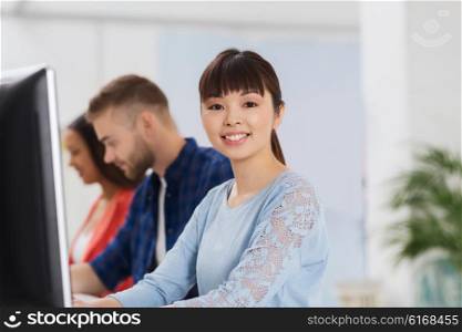 business, startup, education and people concept - happy young asian woman with pc computer over creative team or students working at office