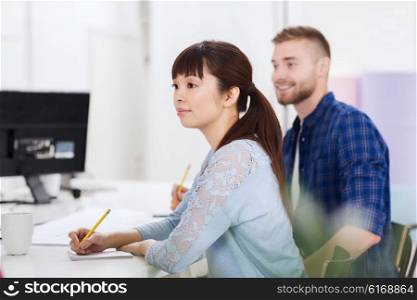 business, startup, education and people concept - happy young asian woman with notebook and pencil over creative team or students working at office