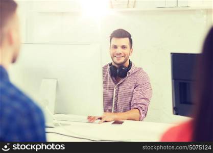 business, startup, education and people concept - happy young creative man with computer and headphones working at office. happy young man or student with computer at office