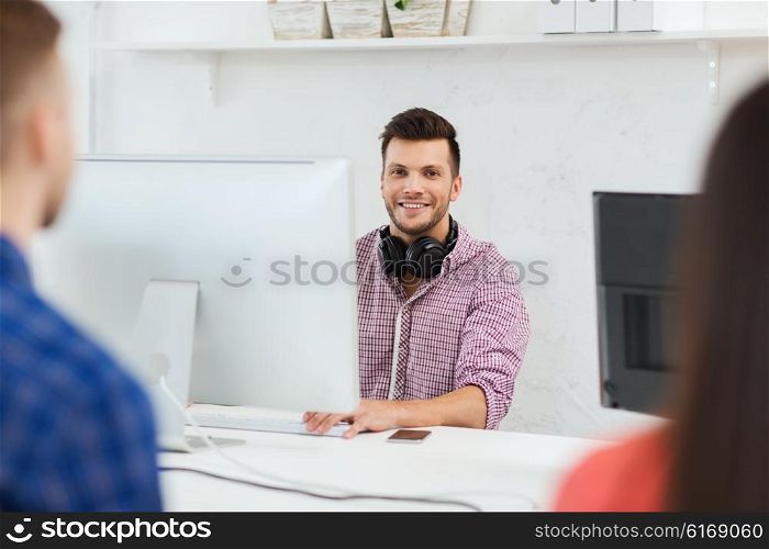 business, startup, education and people concept - happy young creative man with computer and headphones working at office
